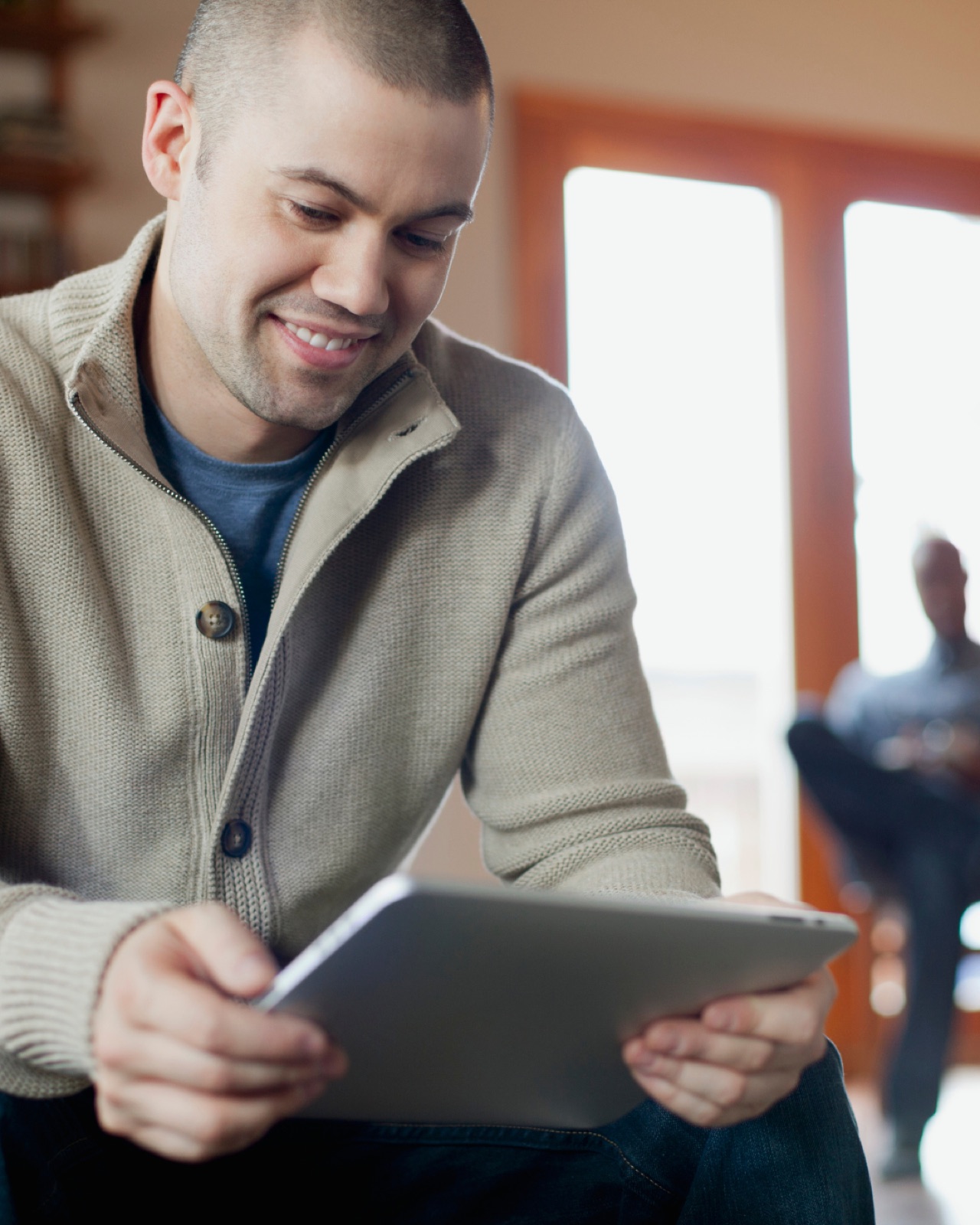 Een man in een beige vest kijkt glimlachend naar een tablet
